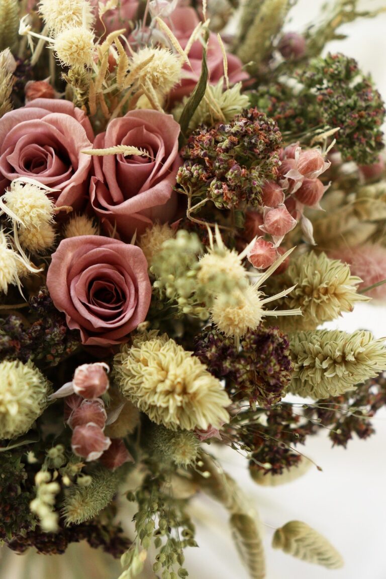This image displays a floral arrangement featuring dusky pink roses, assorted dried flowers and foliage in muted green and pink tones, creating a vintage bouquet.